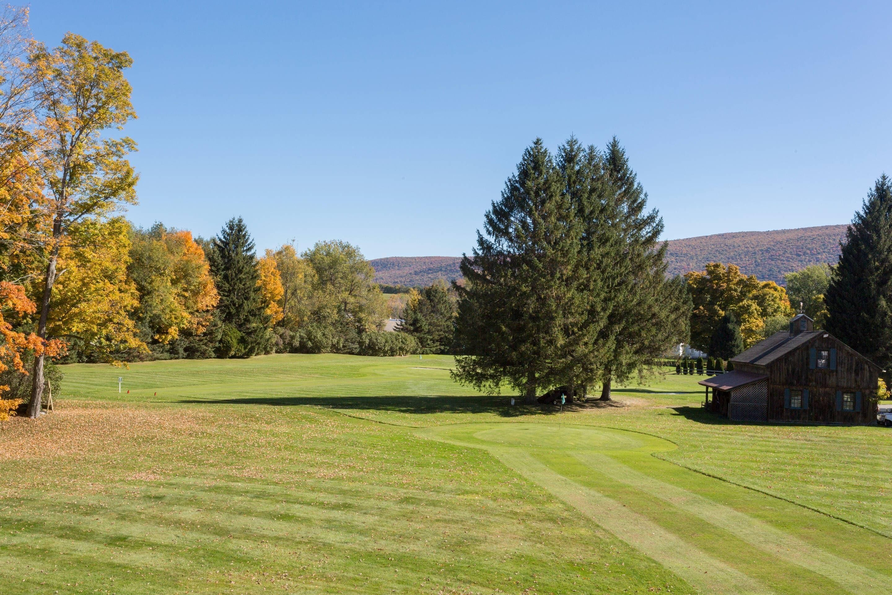 A golf course with a wooden cabin, surrounded by autumn trees and a clear sky.