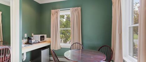 A dining area with a round table and chairs, a microwave, and a small kitchen area with a sink and cabinets.