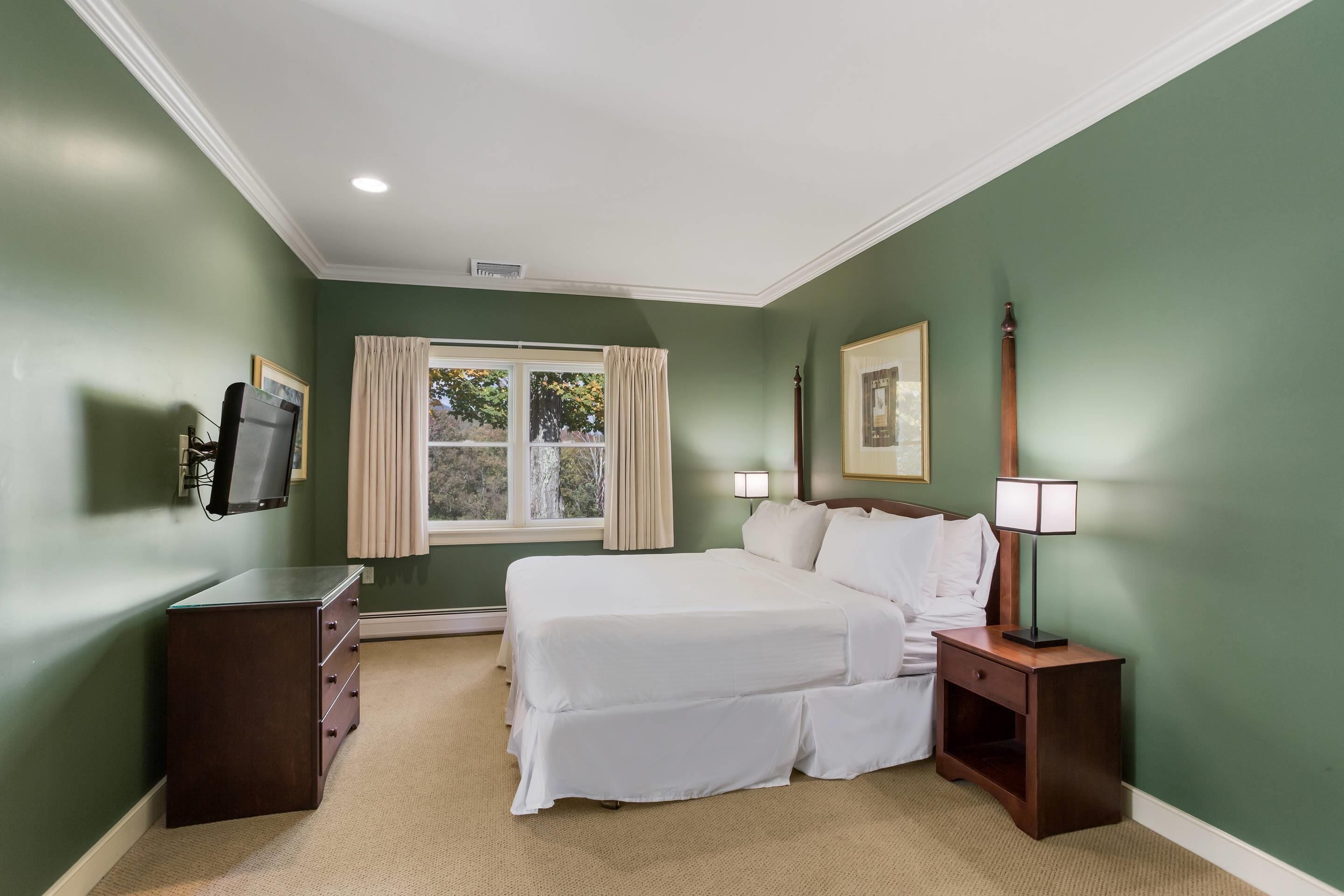 A bedroom with a bed, bedside tables, a TV, and a window with curtains.