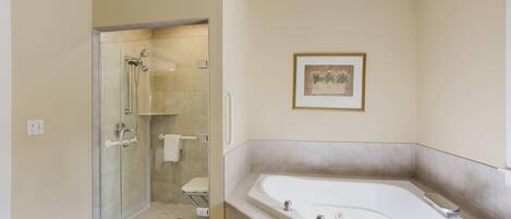 A modern bathroom with a glass-enclosed shower, a large bathtub, and a framed picture on the wall.