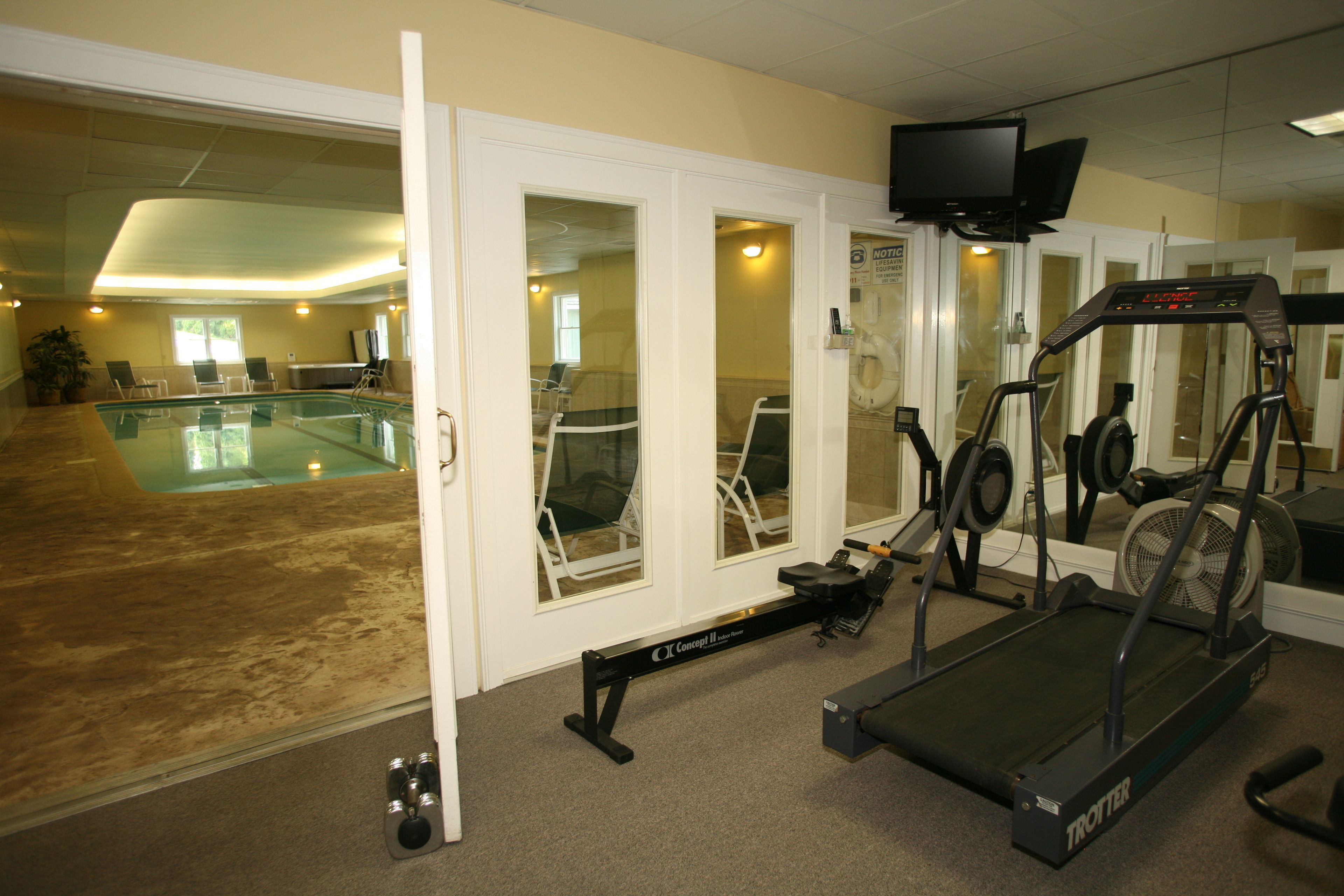 A gym with a treadmill, stationary bikes, and a pool area.
