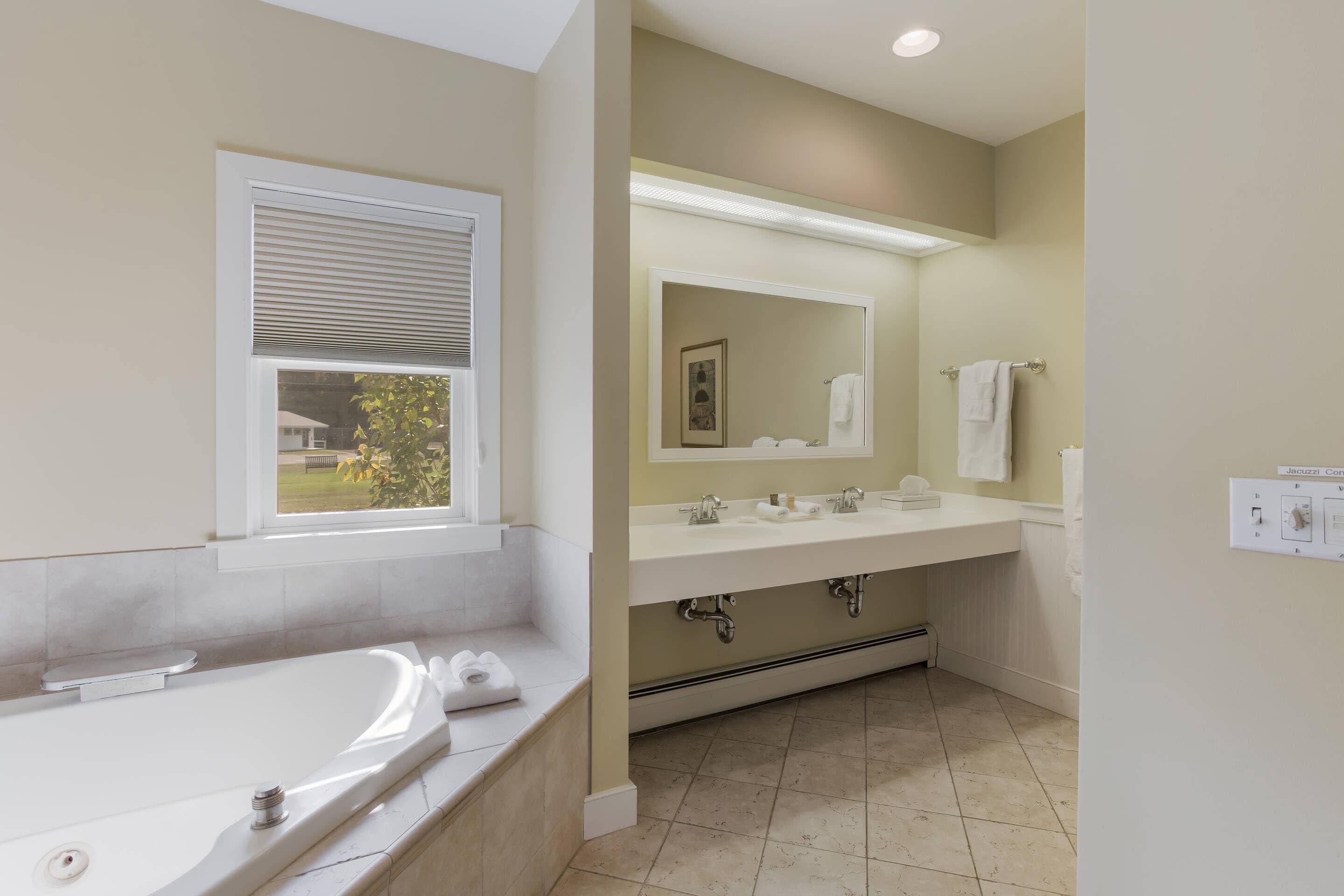A bathroom with a bathtub, two sinks, a large mirror, and a window with blinds.