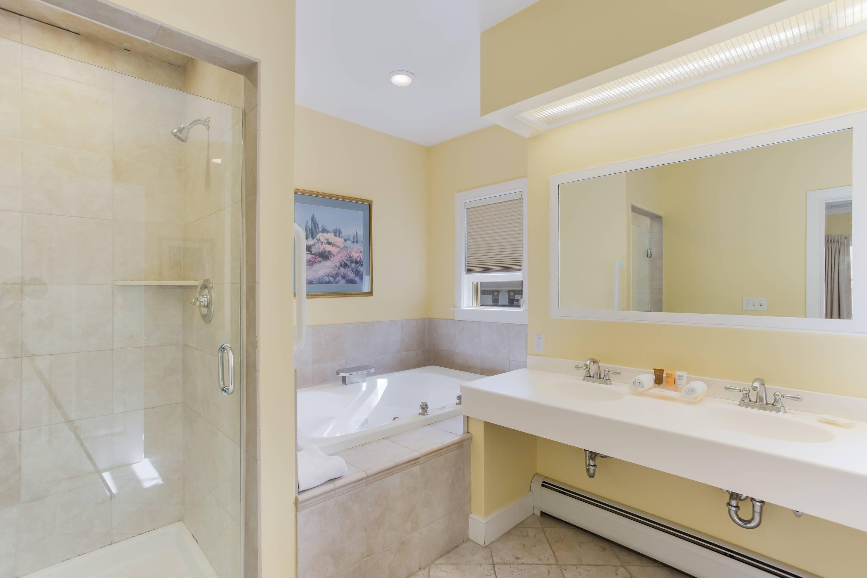 A bathroom with a glass-enclosed shower, a bathtub, and a large mirror above a double sink.