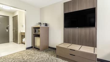 A hotel room with a flat-screen TV mounted on the wall, a wooden cabinet with a microwave, and a patterned carpet.