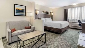 A hotel room with a bed, a sofa, a coffee table, a desk, and a large window with curtains. - Comfort Inn & Suites Pacific - Auburn (Pacific)