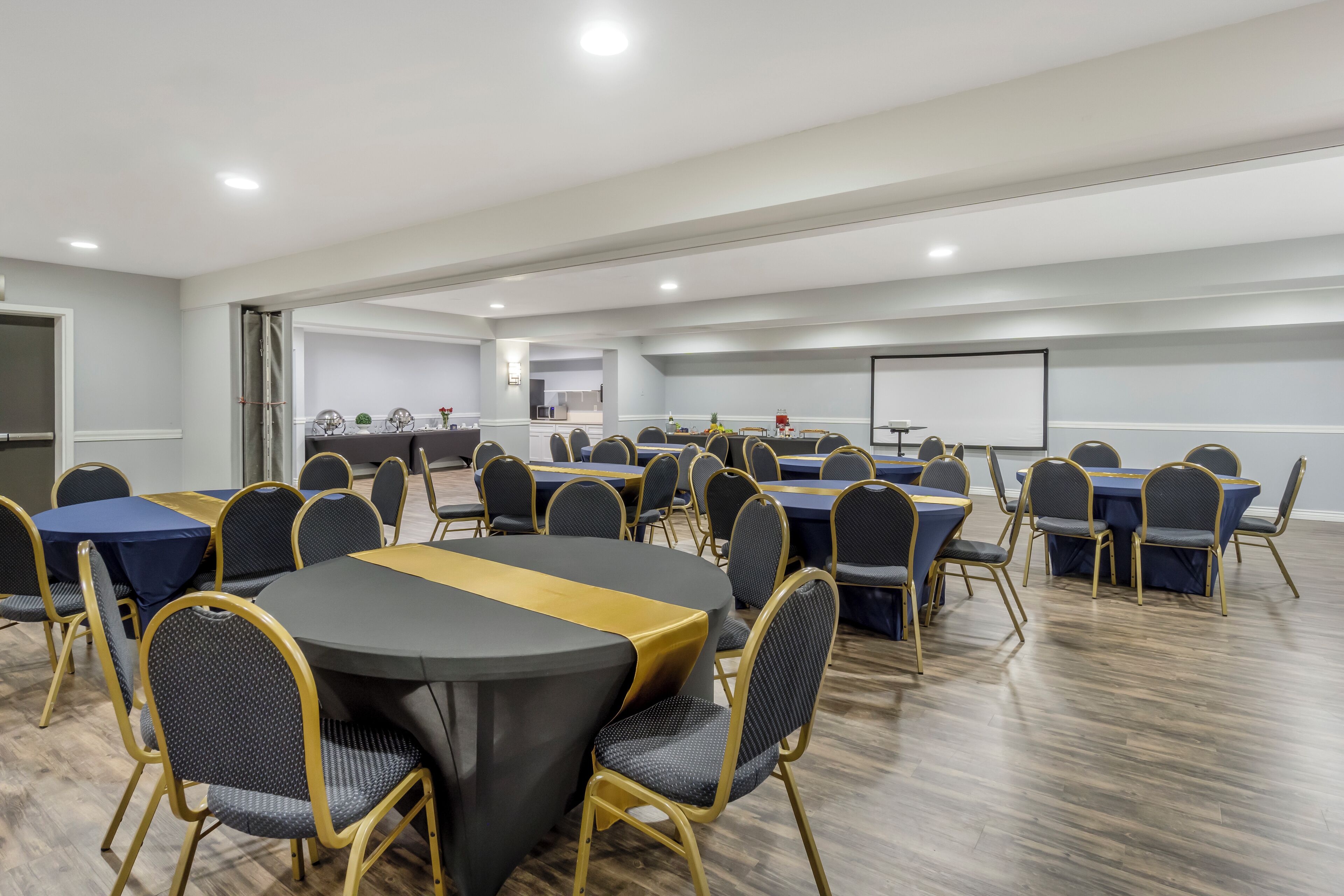 A conference room with round tables and chairs, a whiteboard, and a projector screen.