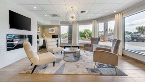 A modern hotel lobby with a large TV, comfortable seating, a decorative chandelier, and large windows offering a view of the parking area. - Comfort Inn & Suites Pacific - Auburn (Pacific)