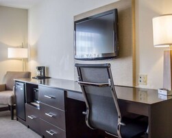 A hotel room with a flat-screen TV mounted on the wall, a foldable desk with a chair, a lamp, and a sofa.