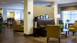 A hotel lobby with a reception desk, seating area with armchairs and sofas, a coffee station, and a large window with curtains.
