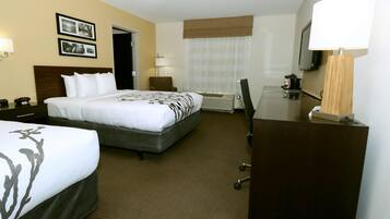Een hotelkamer met een groot bed, een kleiner bed, een bureau, een stoel, een televisie en een lamp.