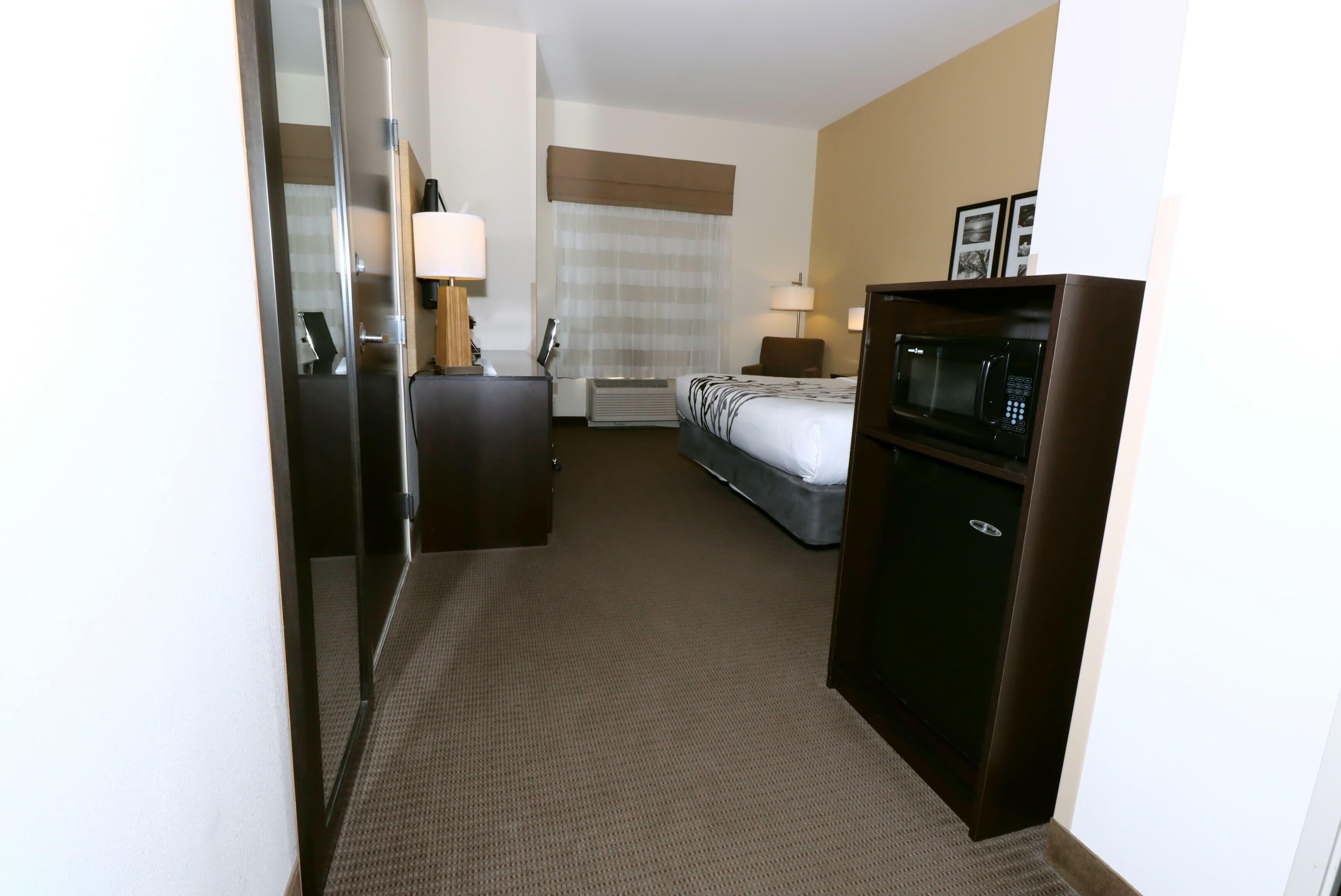 A hotel room with a bed, a desk, a microwave, and a dresser.