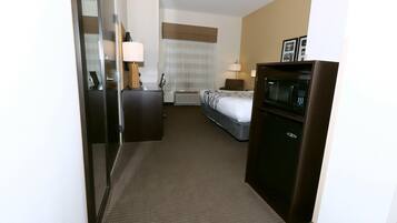 A hotel room with a bed, a desk, a microwave, and a dresser.