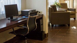 A hotel room with a desk, computer, printer, and two armchairs.