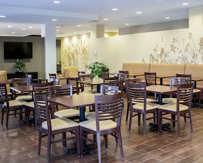 A restaurant with multiple tables and chairs, a sofa, and a TV mounted on the wall.