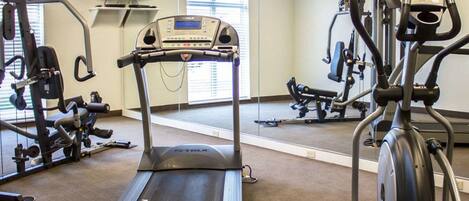 Un gimnasio con caminadora, elíptica y máquinas de pesas.