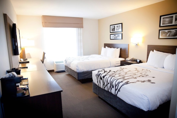 A hotel room with two beds, a desk with a computer, a lamp, and a window with curtains.