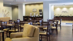 A hotel dining area with multiple tables and chairs, a coffee bar, and a reception desk.