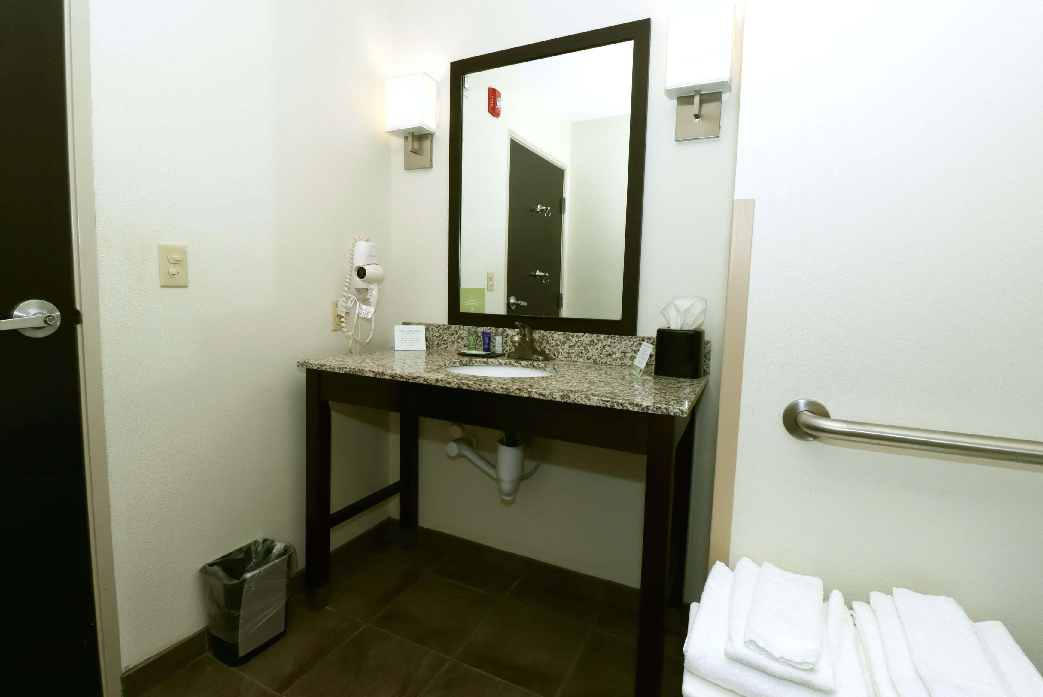 A bathroom with a granite countertop, a sink, a mirror, a towel rack, and a trash bin.