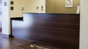 A reception desk with a dark wood finish, a sign for Sleep Inn & Suites, and a welcome mat with a leaf design.