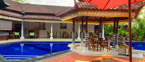 A pool area with lounge chairs and umbrellas, a covered seating area, and a statue.