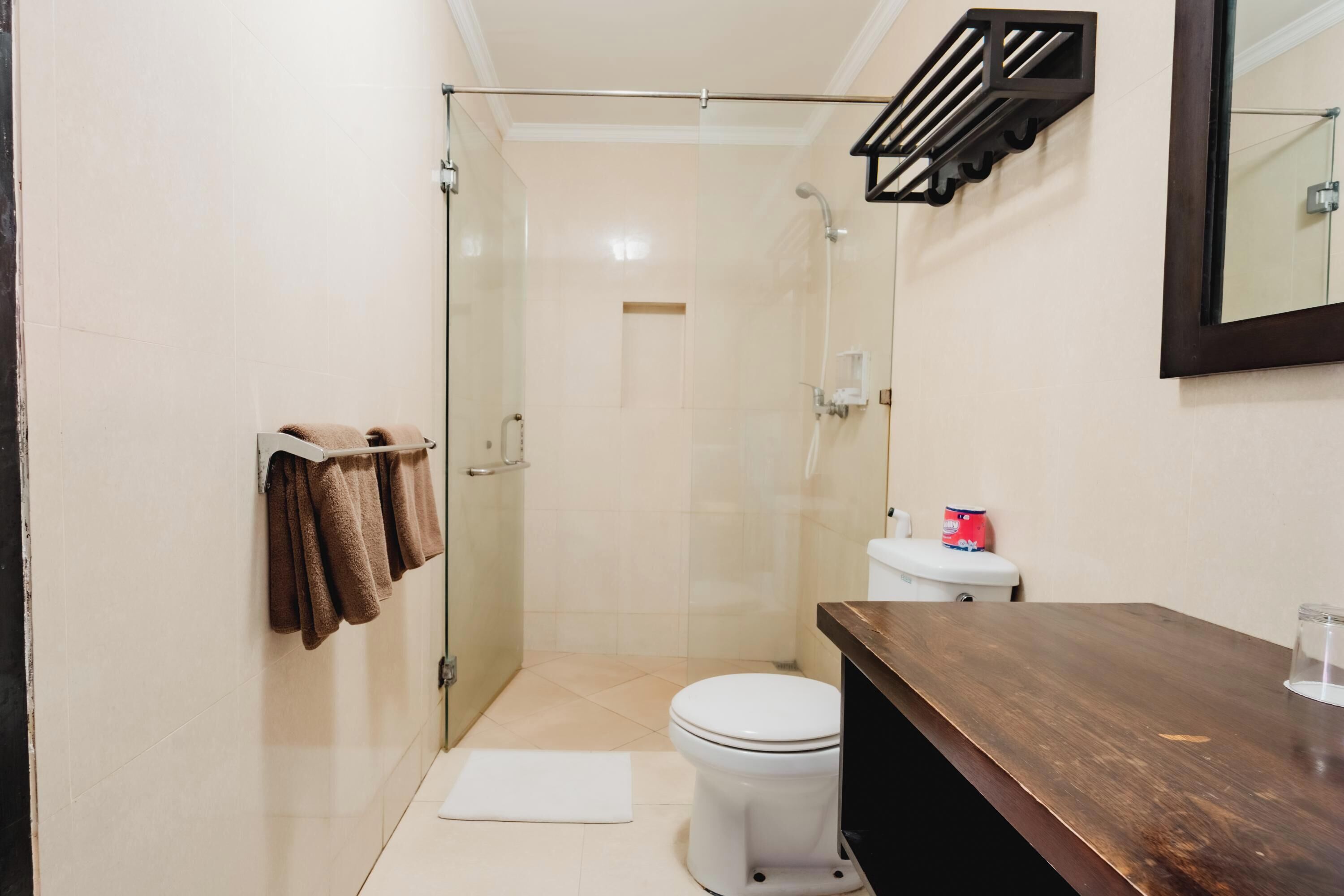 A bathroom with a glass shower enclosure, a toilet, and a wooden vanity.