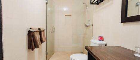 Un baño con cabina de ducha de vidrio, inodoro y tocador de madera.