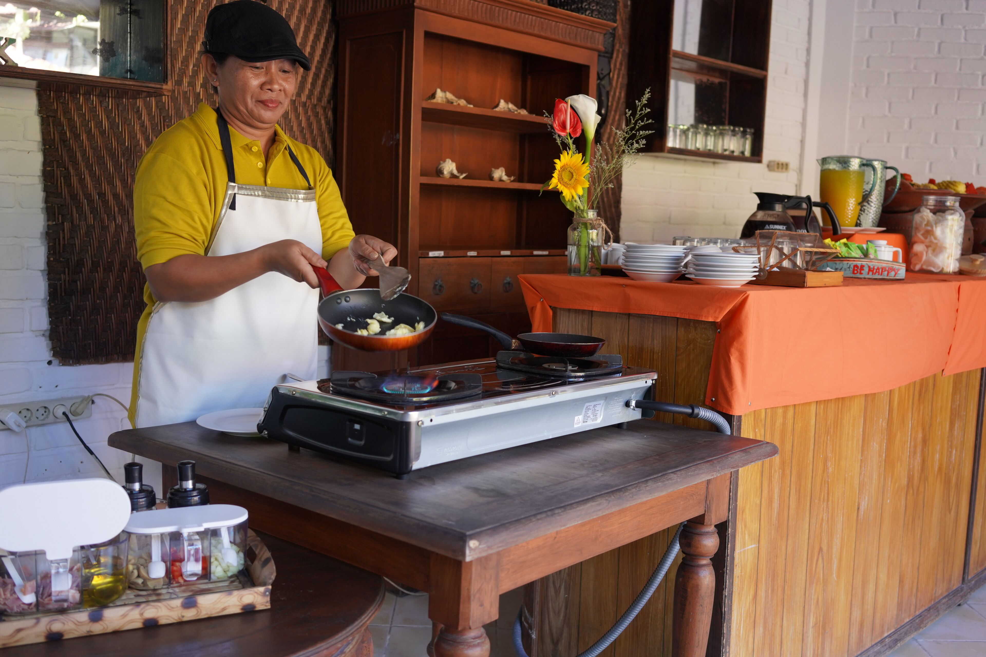 A person cooking on a portable stove with a frying pan, surrounded by kitchen utensils and ingredients.