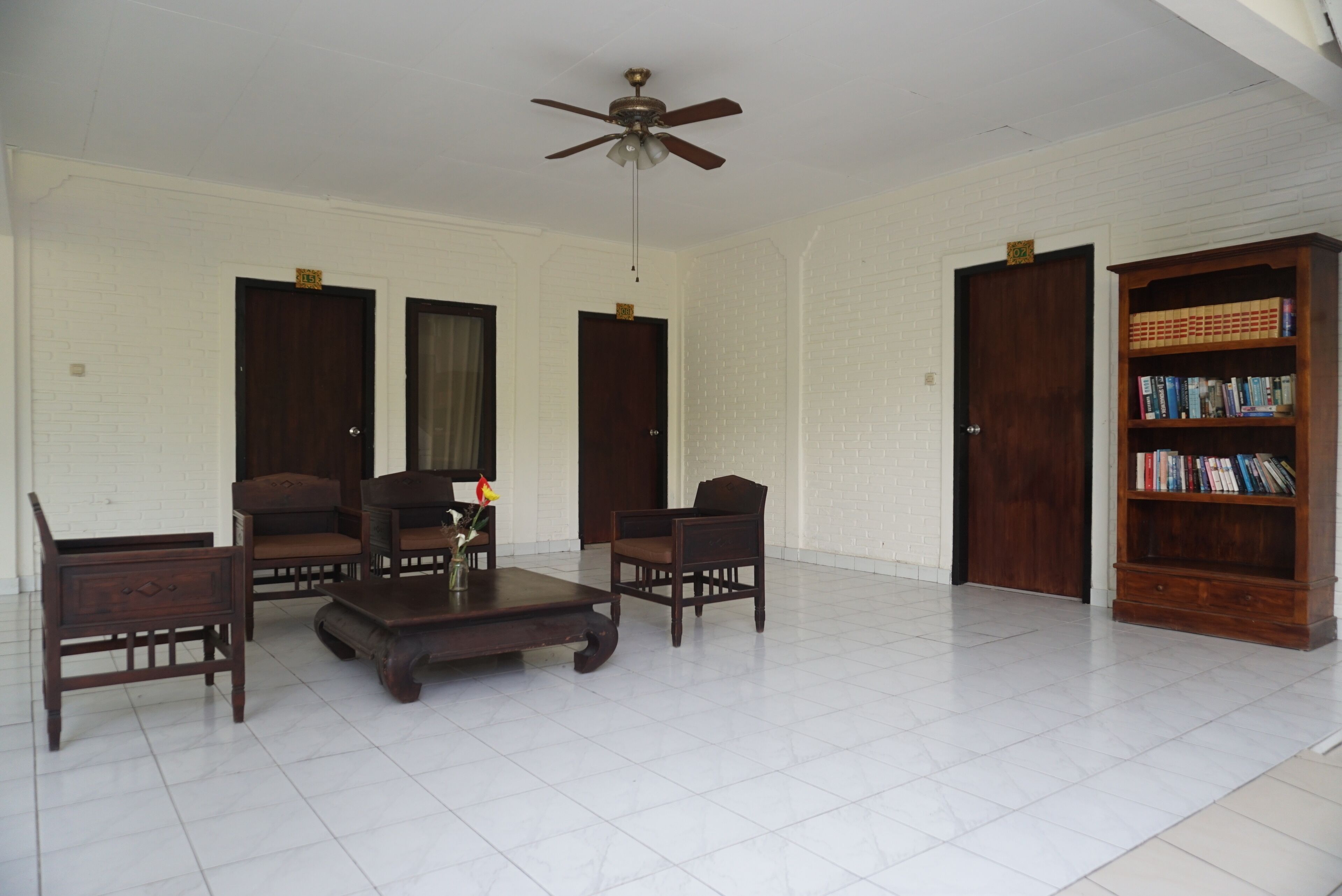 A spacious living room with a ceiling fan, a wooden bookshelf, and a white brick wall.