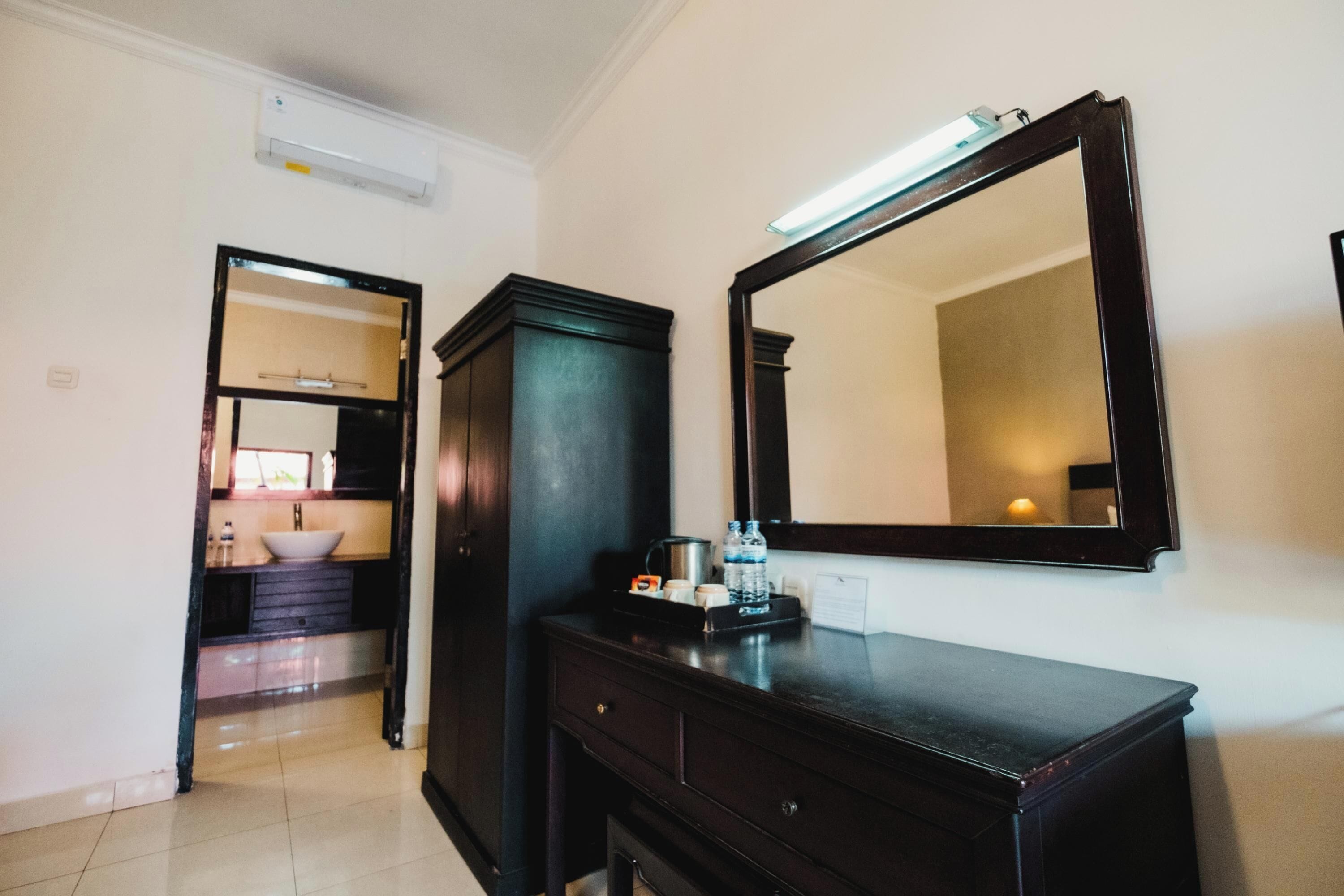 Une chambre d’hôtel avec une commode en bois foncé, un grand miroir et une petite table sur laquelle se trouvent une bouteille d’eau et une tasse.