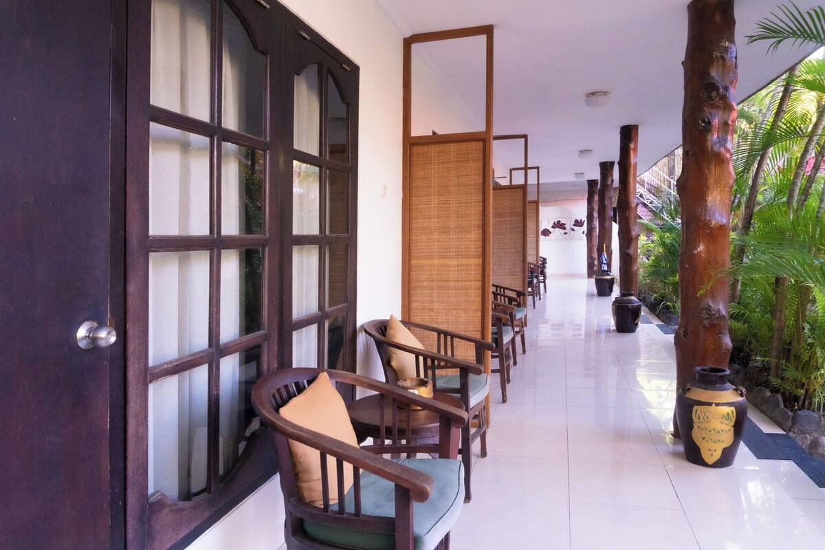 A corridor with wooden chairs and a bamboo screen, leading to a room with a large wooden door.