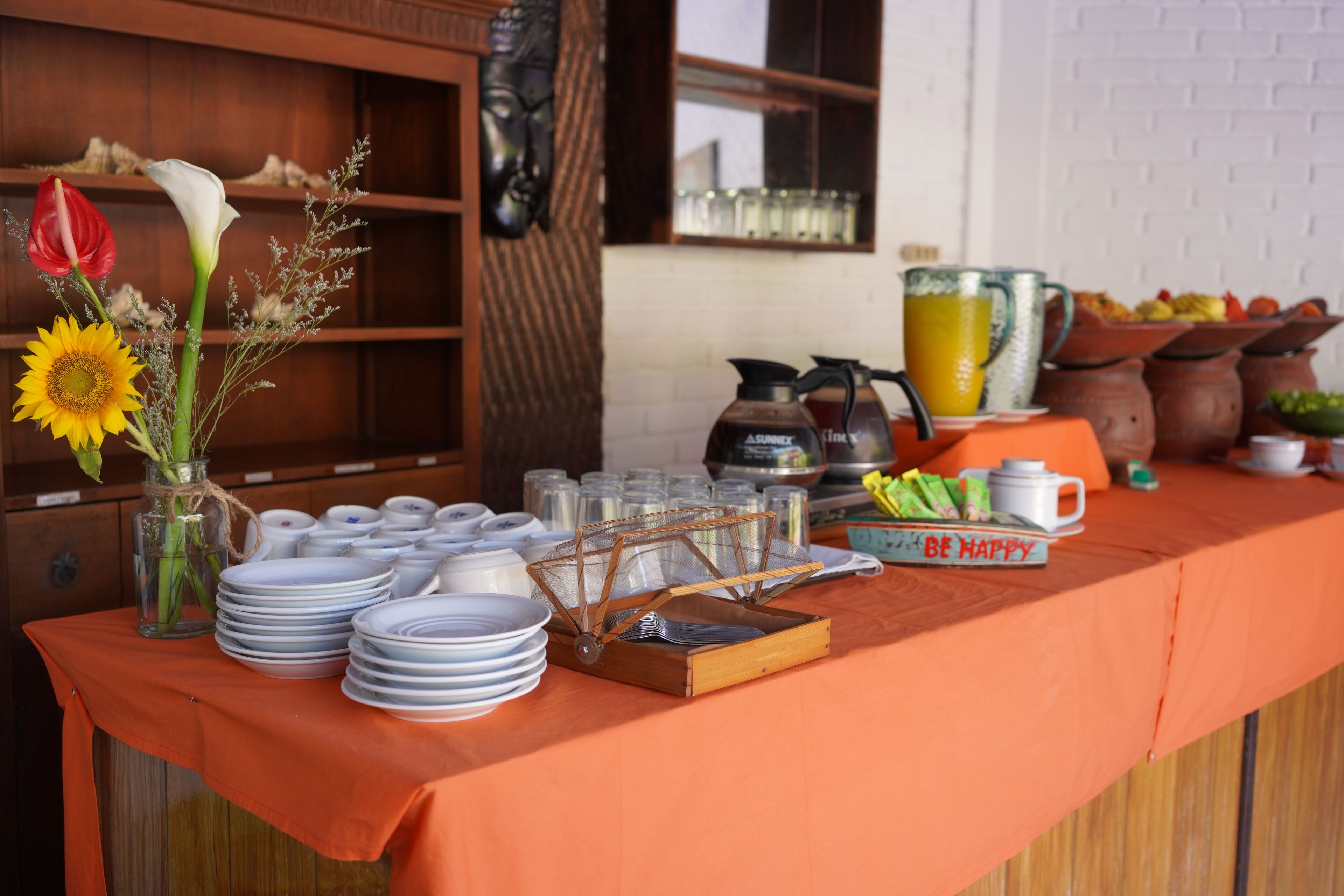 A buffet table with plates, a pitcher, and a 'BE HAPPY' sign.