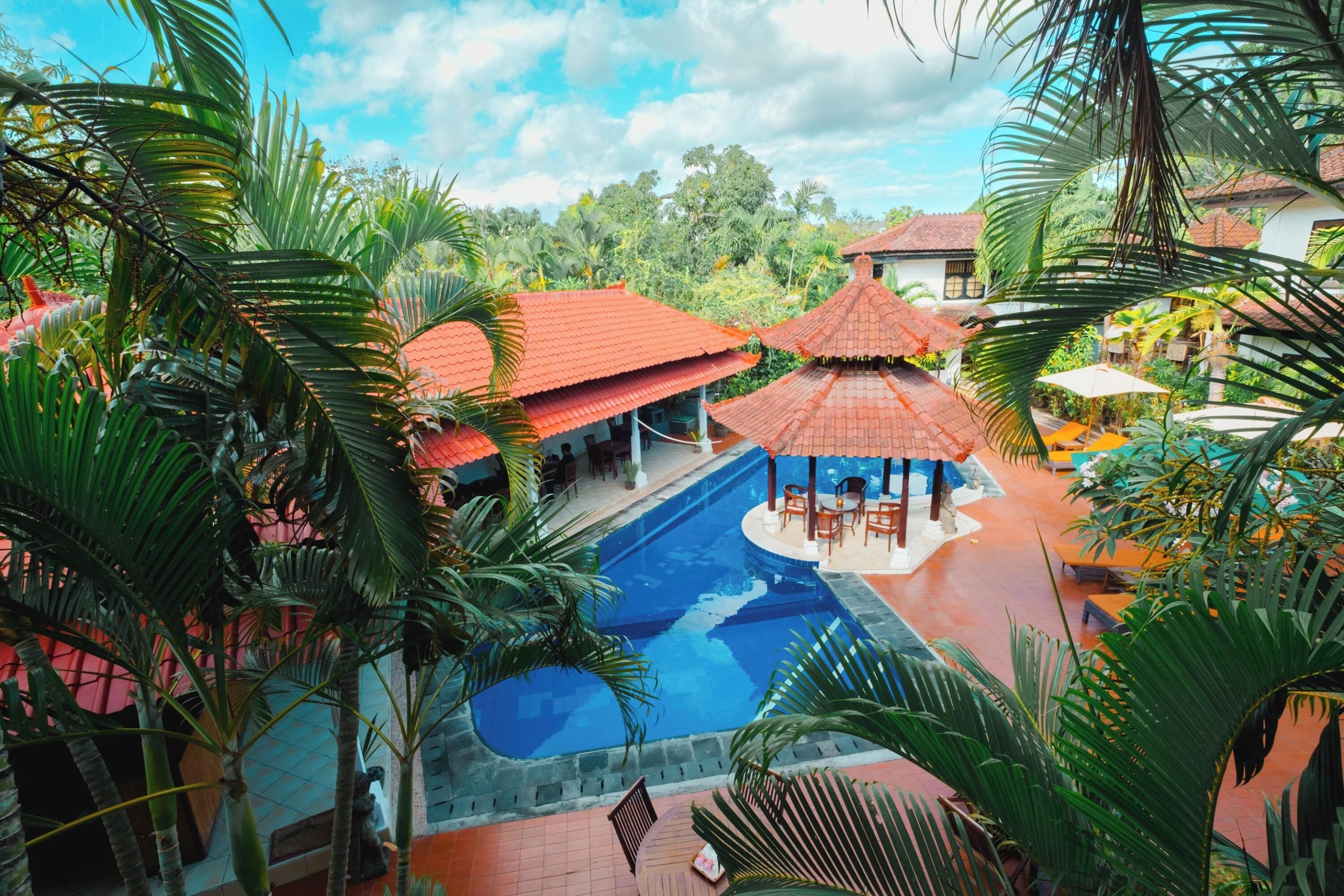 A pool area with a red-roofed pavilion, surrounded by palm trees and a view of the landscape.