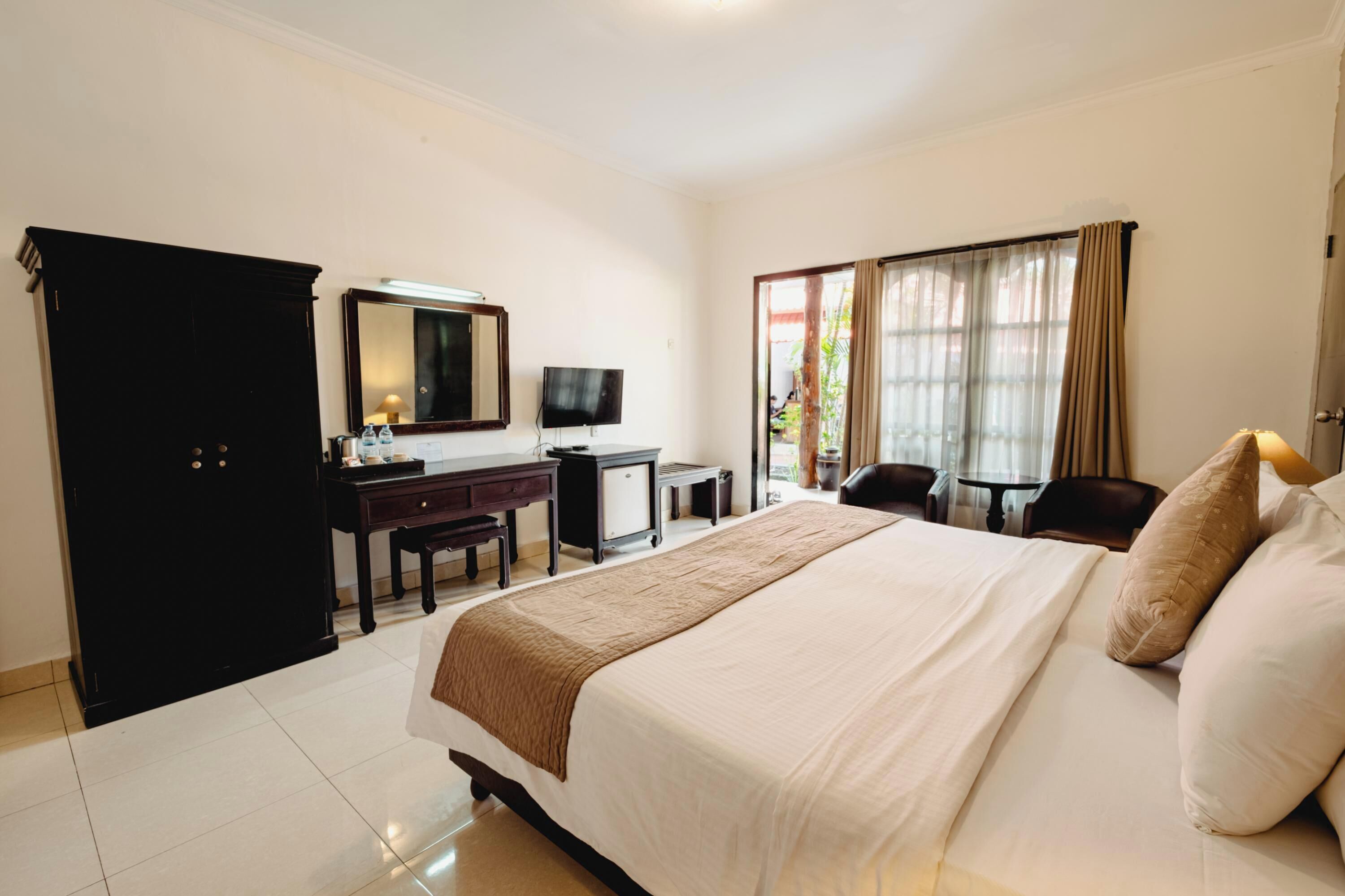 Una habitación de hotel con una cama grande, un escritorio con computadora, una silla, un armario y una ventana con cortinas.
