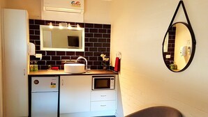 A compact kitchen with a refrigerator, microwave, sink, and a mirror on the wall. - Bidgee Motor Inn (Hay)