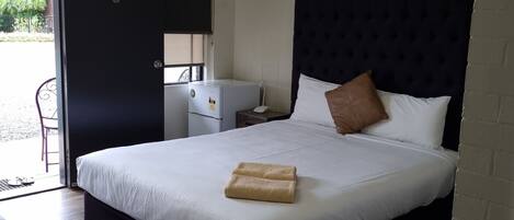 A hotel room with a large bed, a small desk, a chair, and a door leading to a balcony.