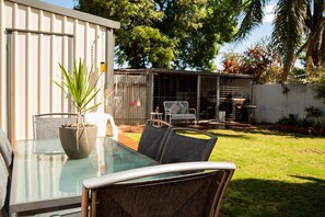 A glass-top table with chairs, a potted plant, and a fenced outdoor area with a patio set.