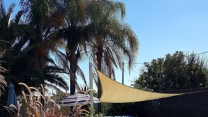 A poolside area with a chair, a table, and a shade sail. - Bidgee Motor Inn (Hay)