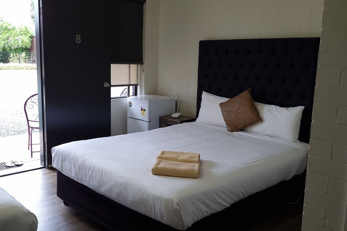 Habitación de hotel con una cama grande, un escritorio pequeño, una silla y una puerta que da a un balcón.
