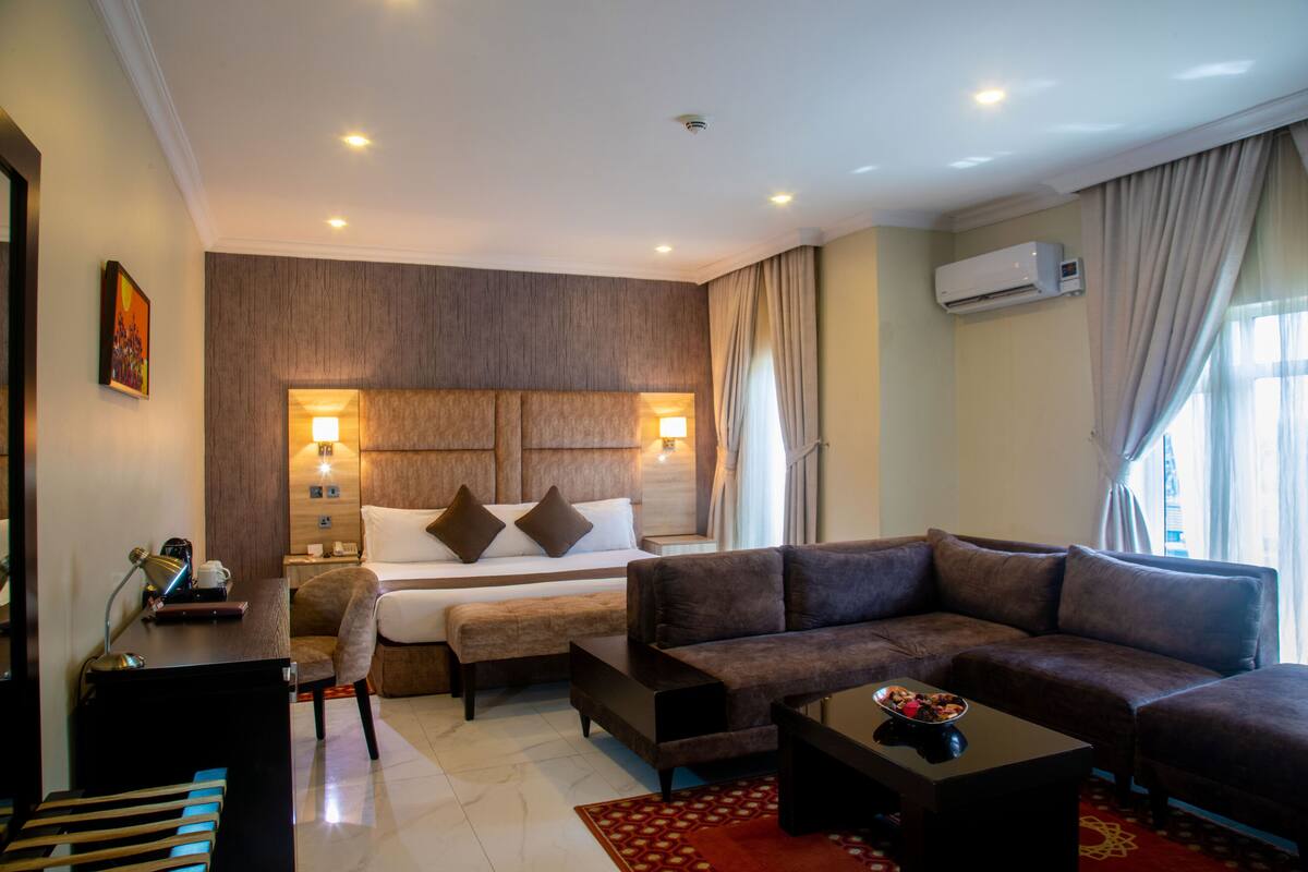 Habitación de hotel con cama, sofá, escritorio y un gran ventanal con cortinas.