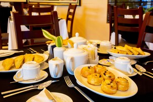 Una mesa de desayuno con diversos pasteles, teteras, tazas y cubiertos.