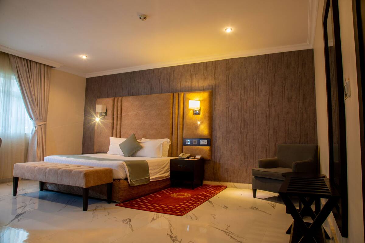 Una habitación de hotel moderna con una cama grande, mesitas de noche, una silla y una alfombra roja.