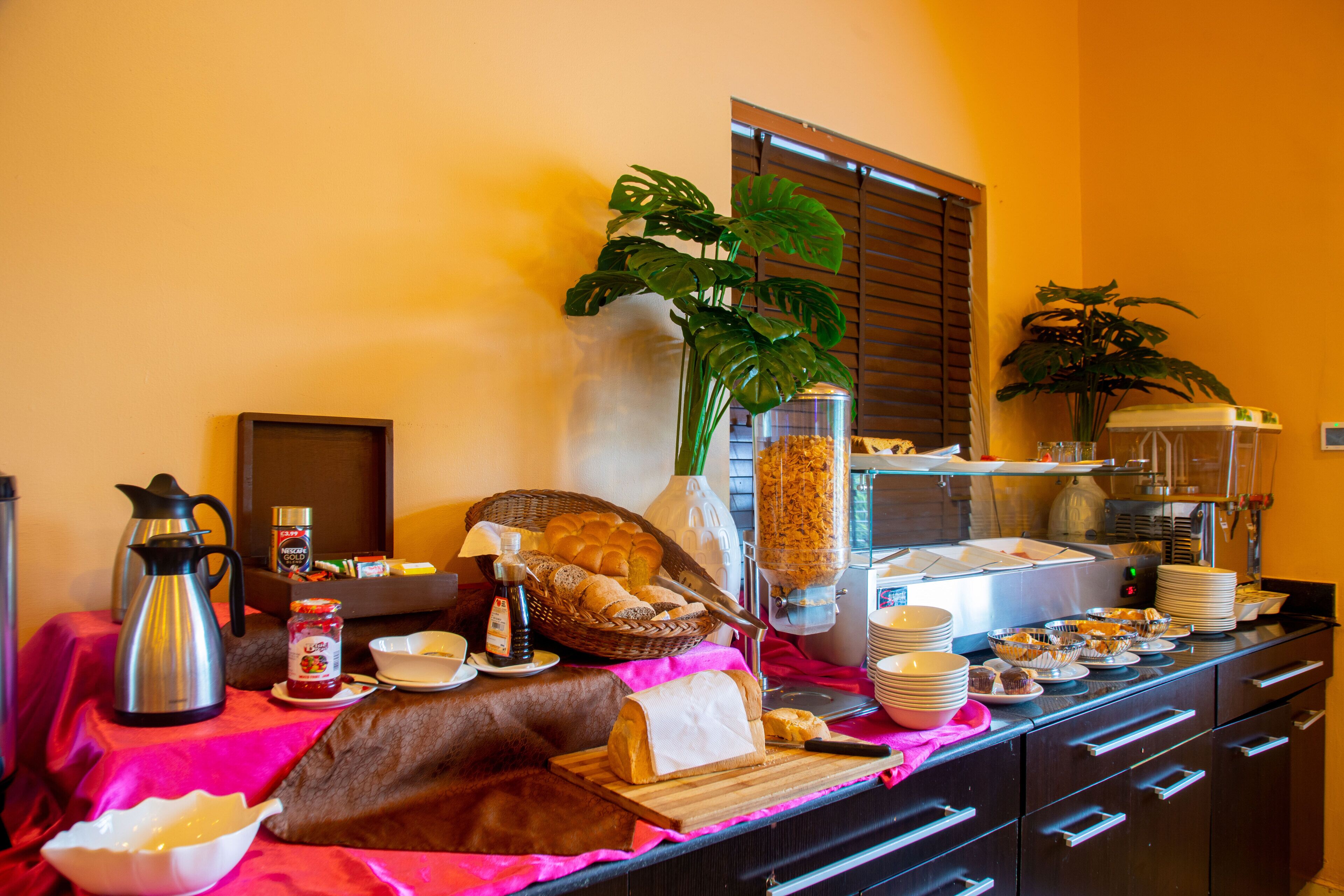 A buffet setup with various food items, a coffee pot, and a plant.