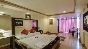 Habitación de hotel con una cama grande, un escritorio con lámpara, una silla y un área de comedor con mesa y sillas.