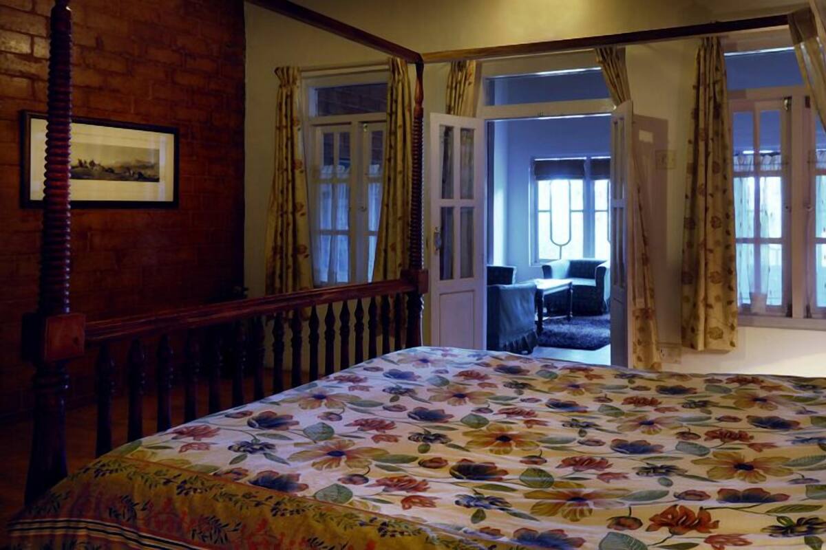 Un dormitorio con colcha estampada, cabecera de madera y vista a un balcón con una silla.