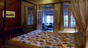 Un dormitorio con colcha estampada, cabecera de madera y vista a un balcón con una silla.