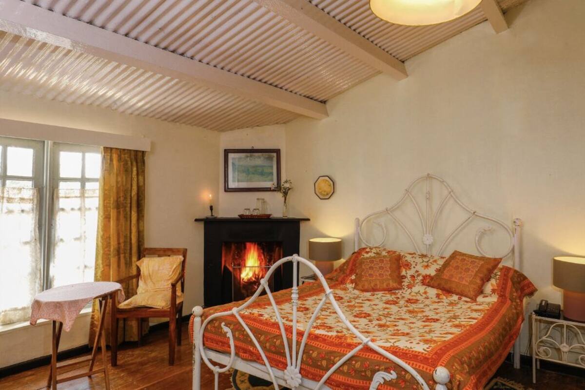 Un dormitorio acogedor con una cama de metal blanco, una chimenea, una mesita pequeña y una silla.
