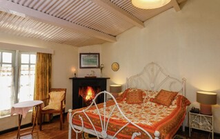 A cozy bedroom with a white metal bed, a fireplace, a small table, and a chair.
