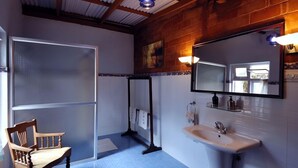 Une salle de bain avec une grande fenêtre, une chaise en bois, un lavabo et un miroir.