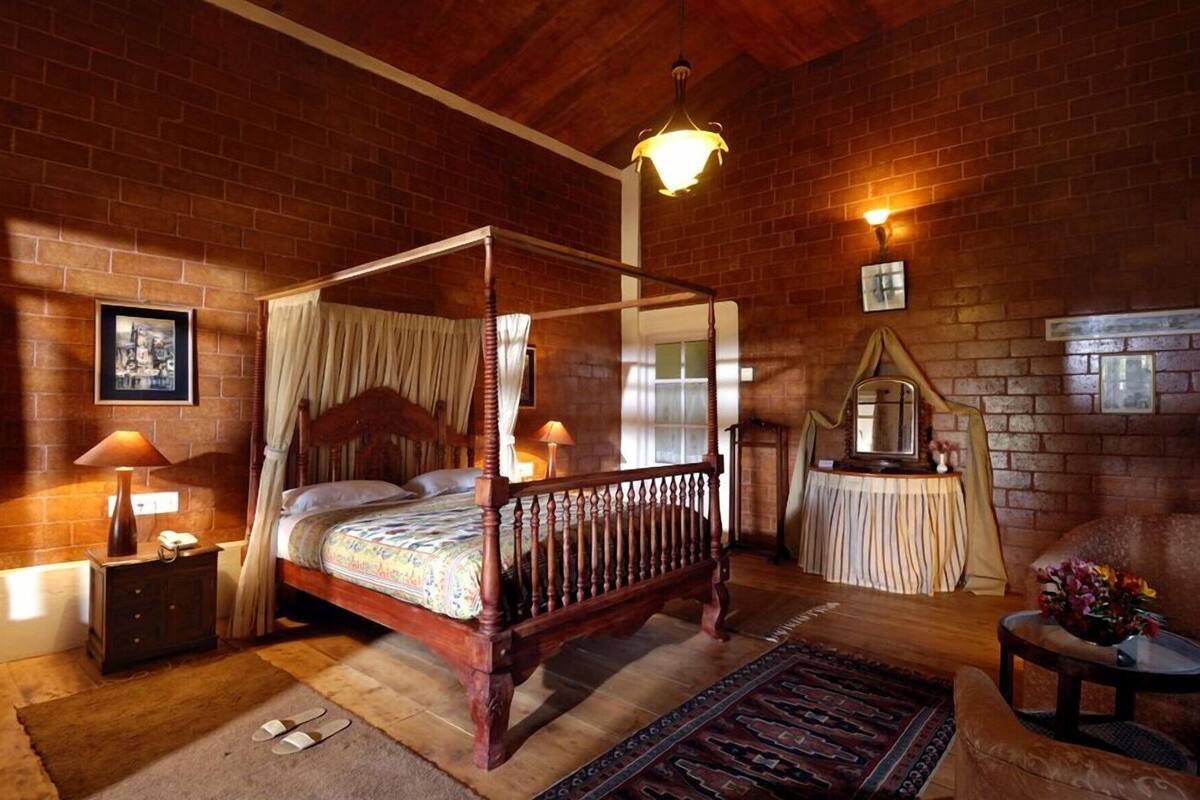 Una cama con dosel en una habitación rústica con paredes de ladrillo, techo de madera y un candelabro.