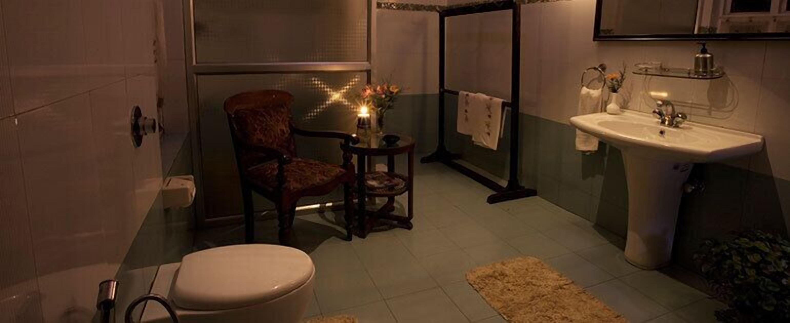 A bathroom with a toilet, a sink, a chair, and a mirror.